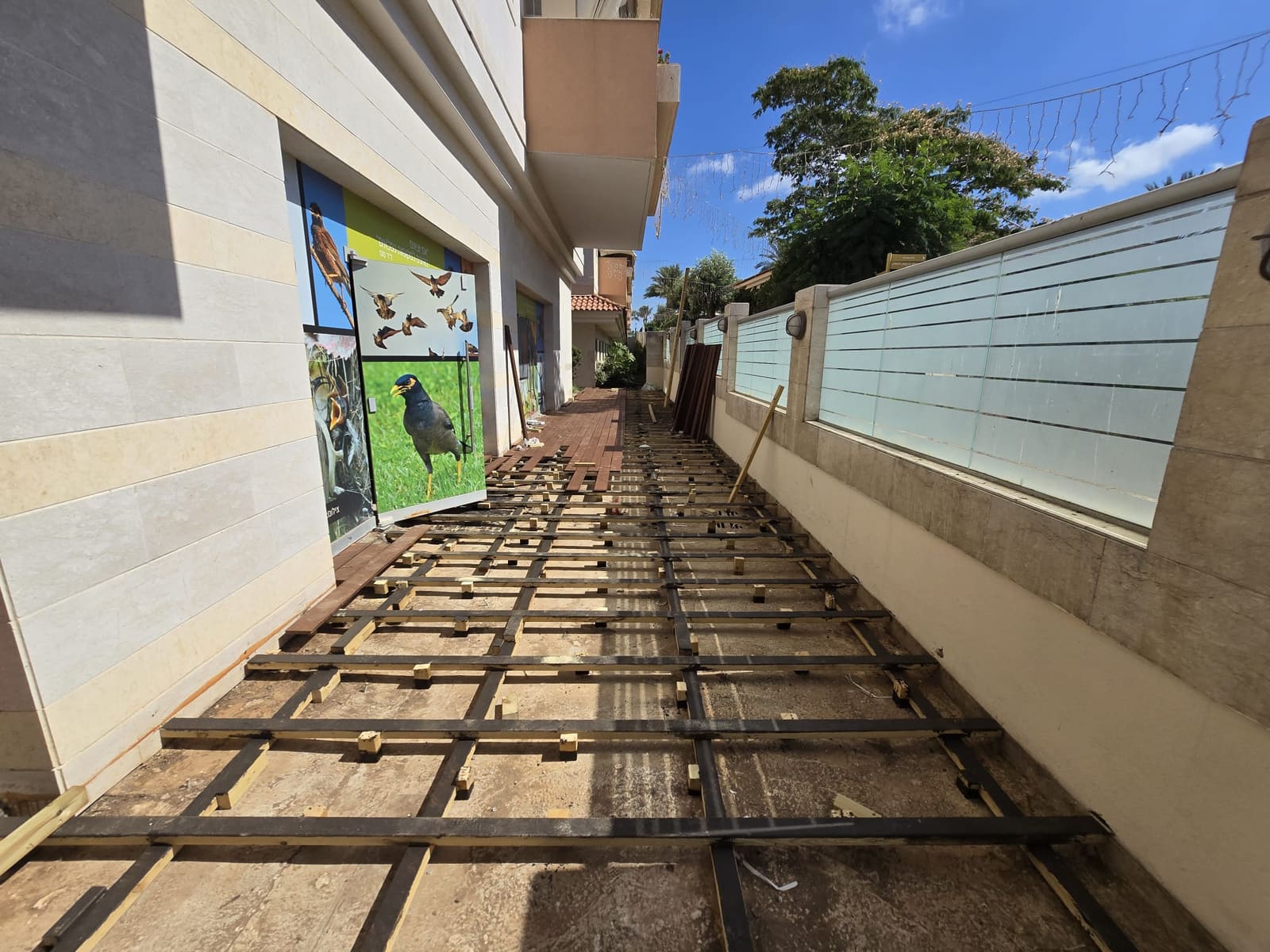 פרופילי פלדה שחורים מונחים על רצפת בטון לאורך מעבר, עם טריזי עץ קטנים ביניהם