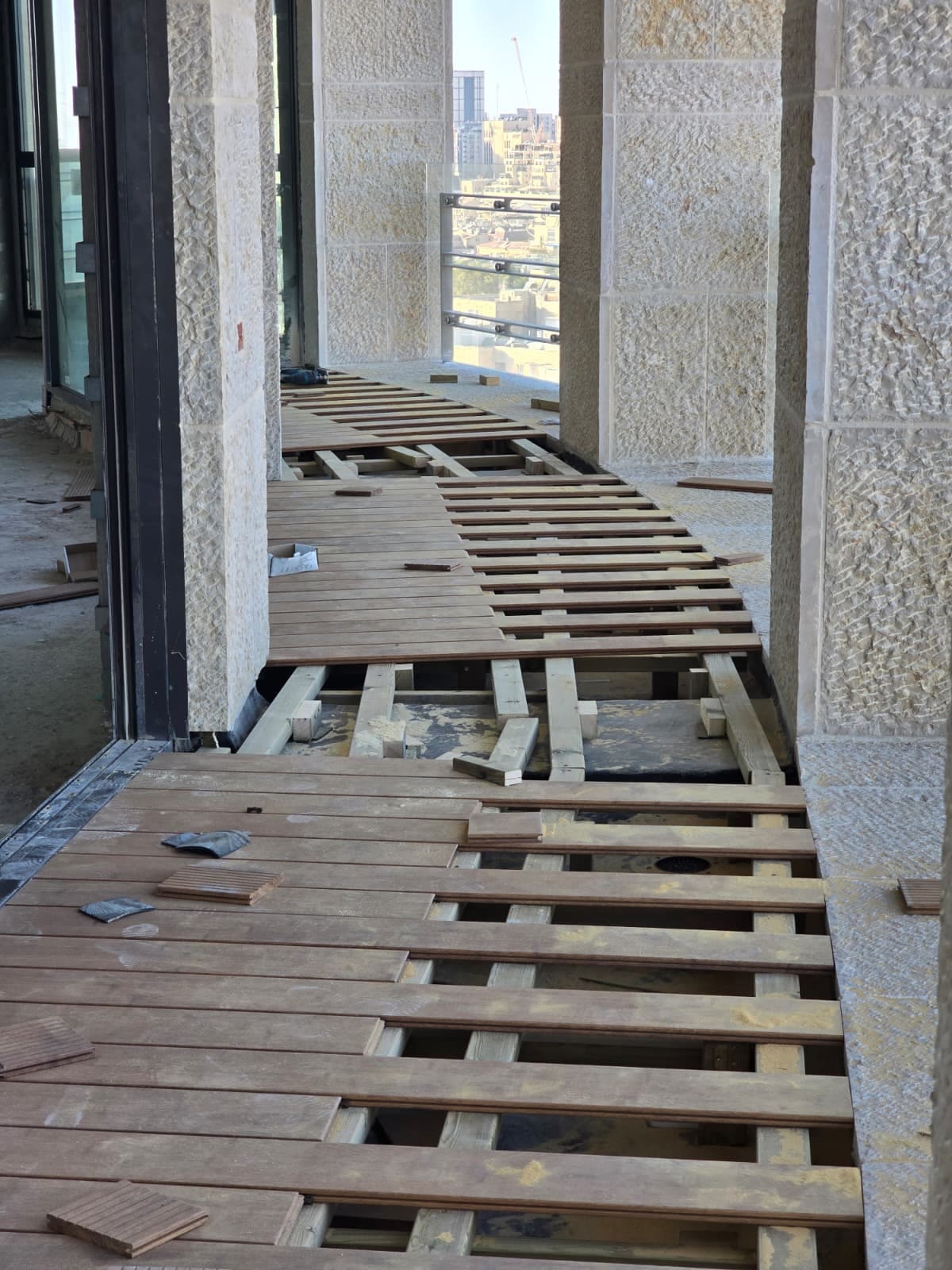 לוחות עץ קשה מונחים באלכסון מעל שלד קורות פתוח במרפסת צרה בין עמודי אבן