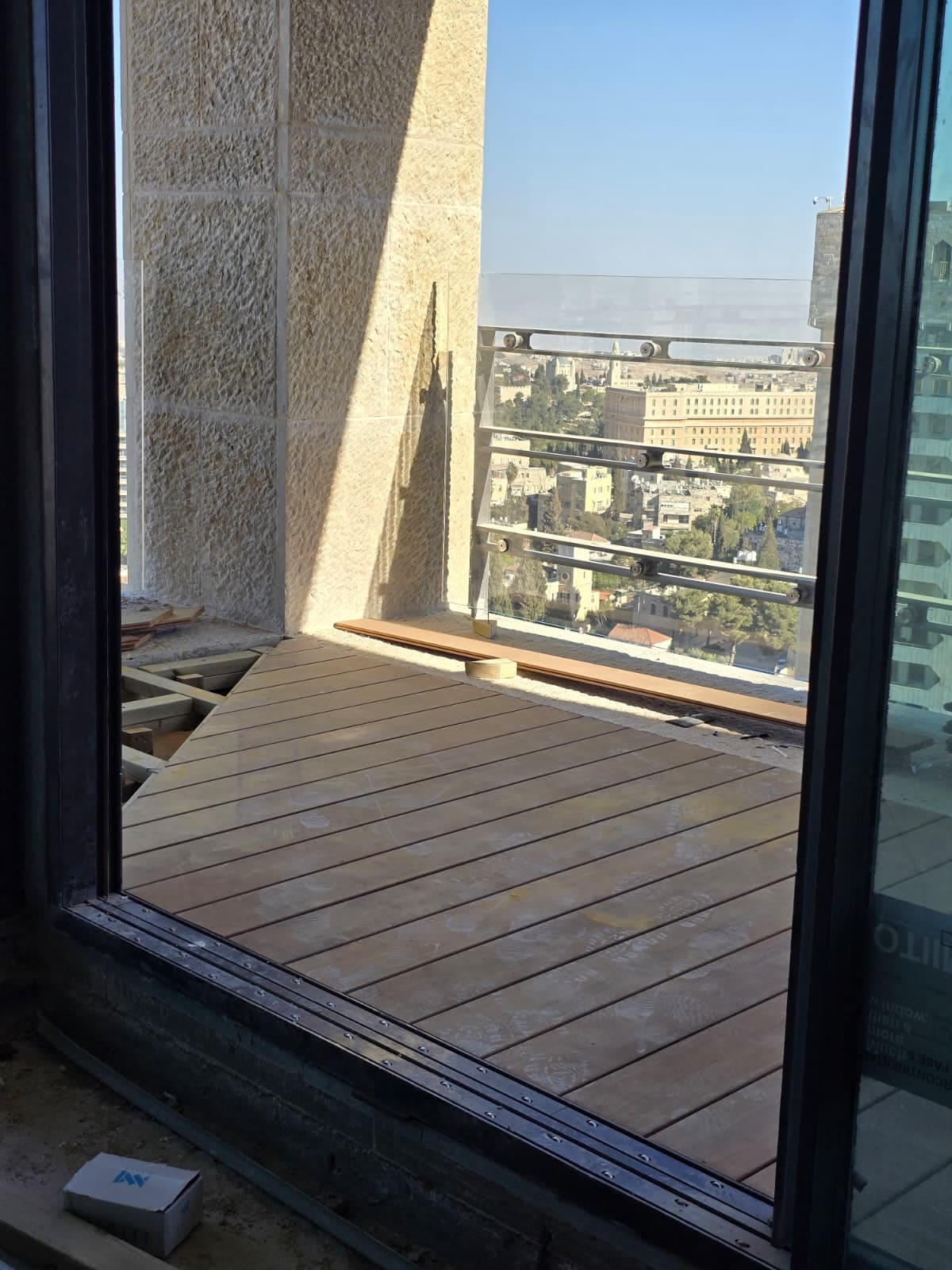 דק עץ כהה מוגמר במרפסת פנטהאוז, נפגש עם רצועת אבן בשוליים, מול נוף אבן ירושלמי